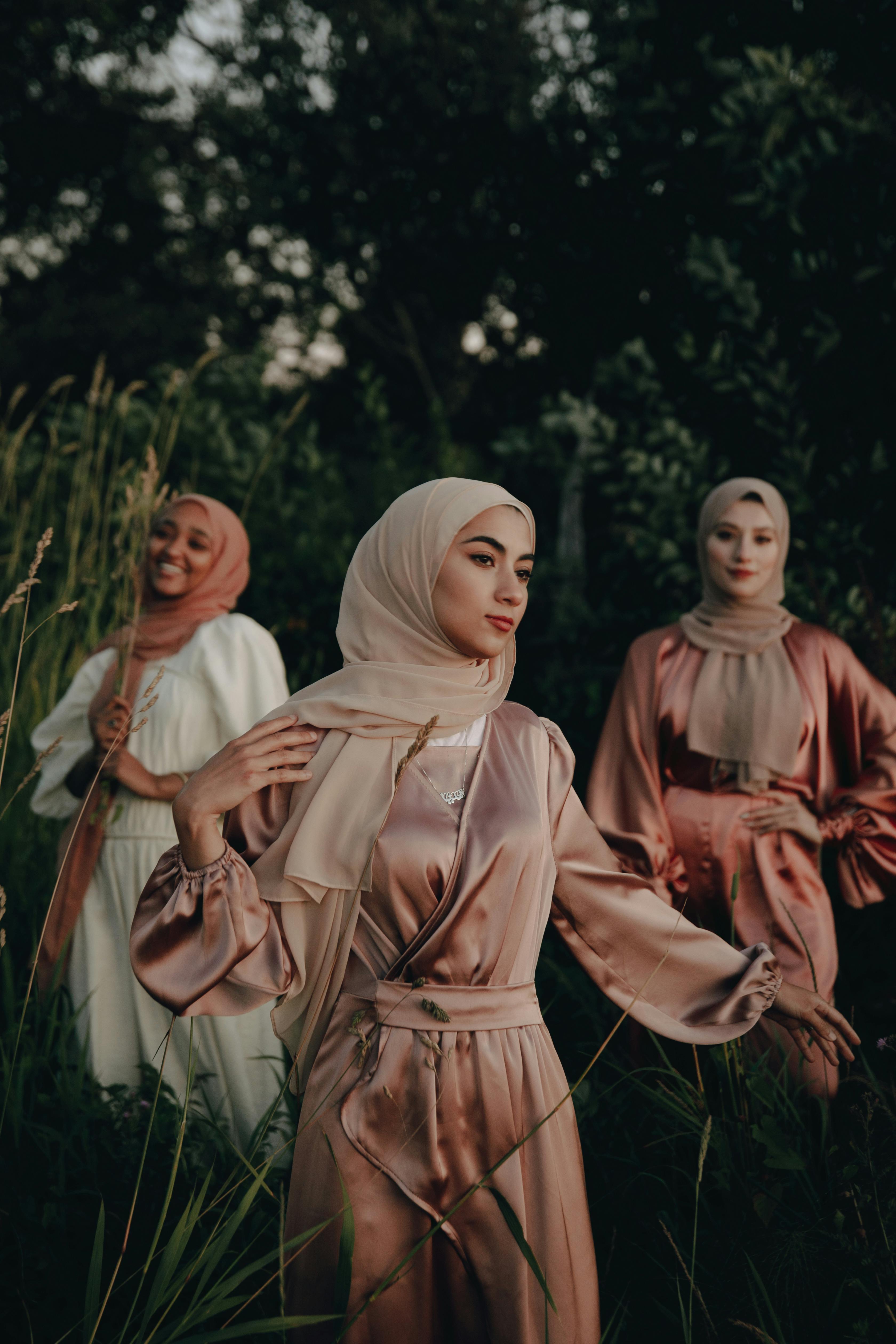 Three hijabi women in matching outfits with hijabs standing in a natural setting.
